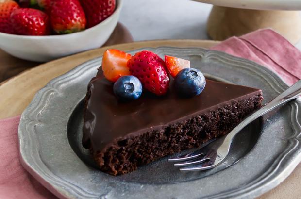 Slice of luscious flourless chocolate cake with ganache topped with berries