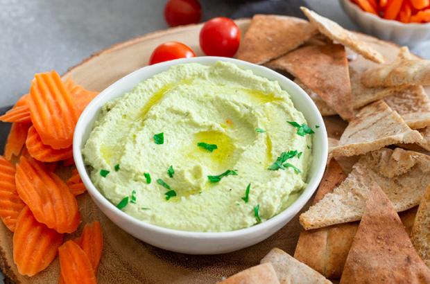 Bowl of green hummus with baked pita chips